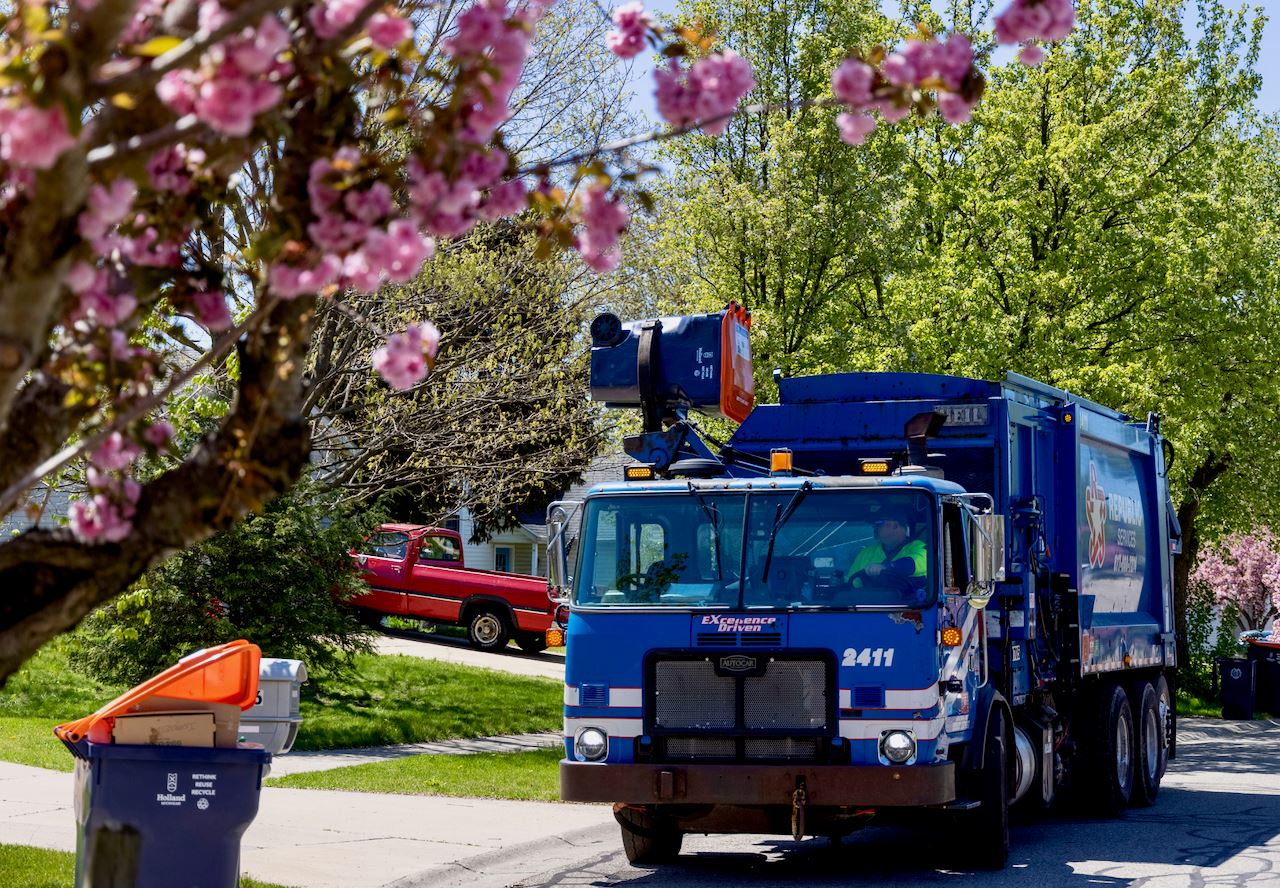 front of recycling truck lifting a recycing bin into the back of the truck