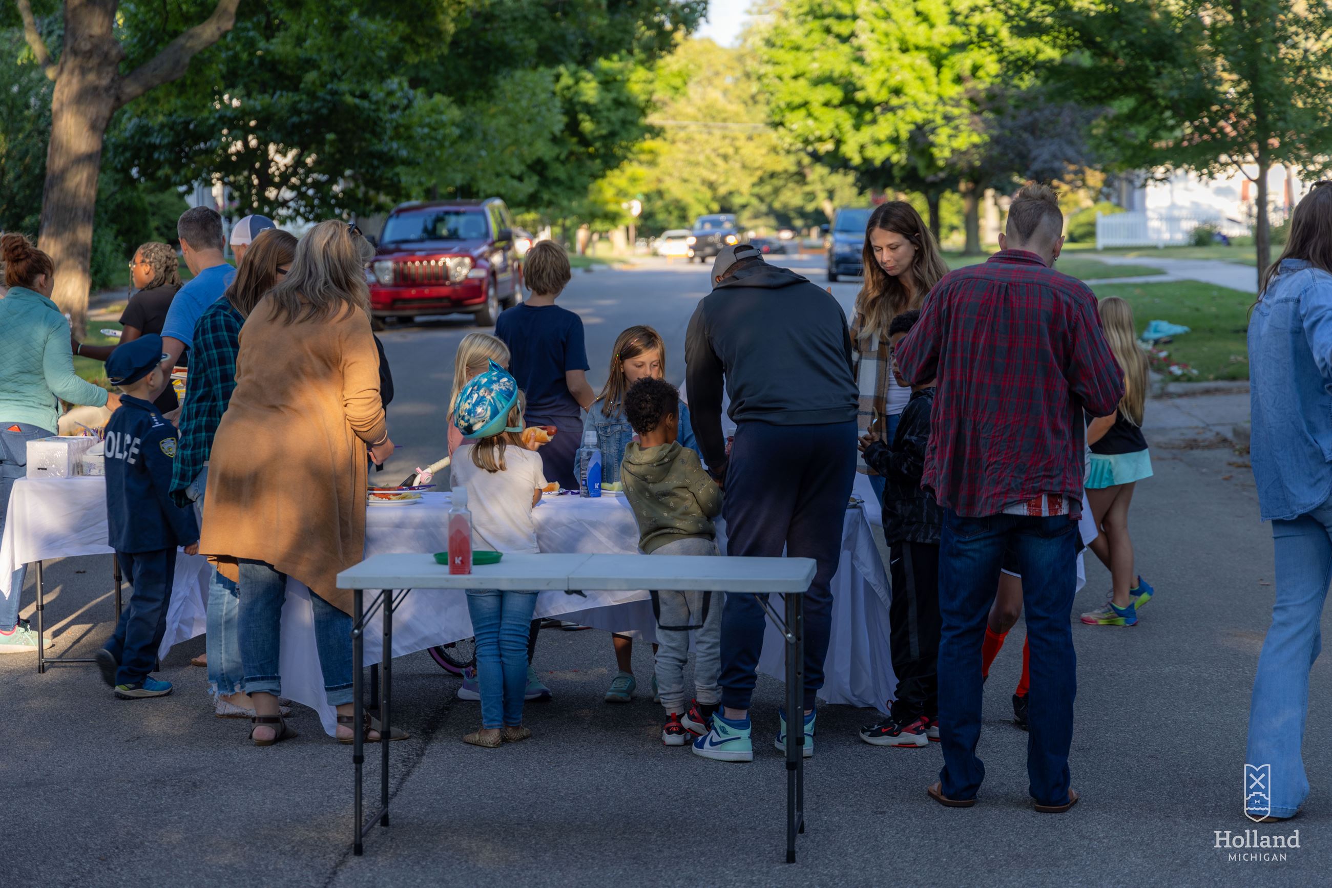 Neighbors gathered in a residential street for a block party. Table with food in forground