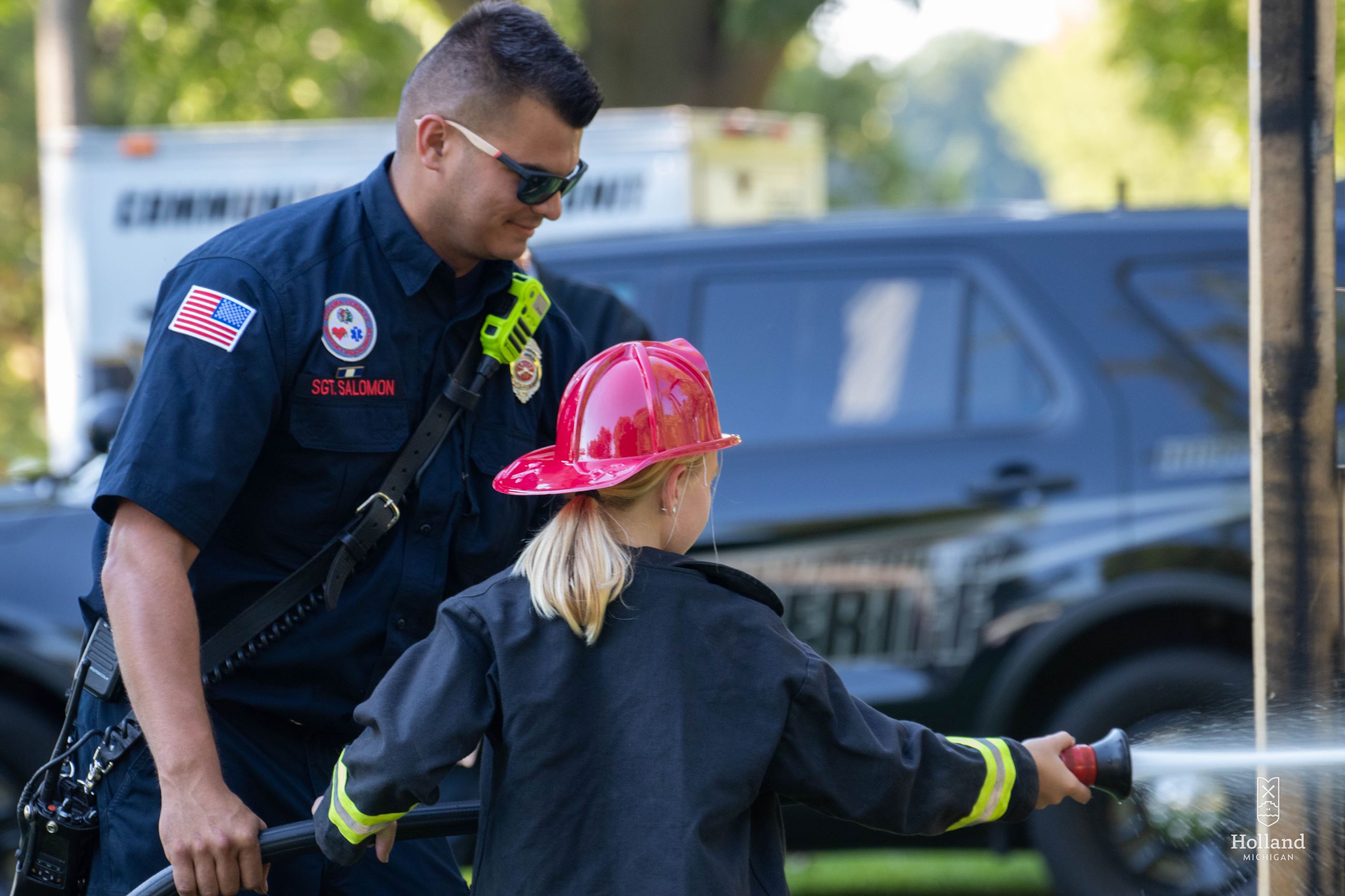 Firefighter helping a young girl test a fire hose at a community event