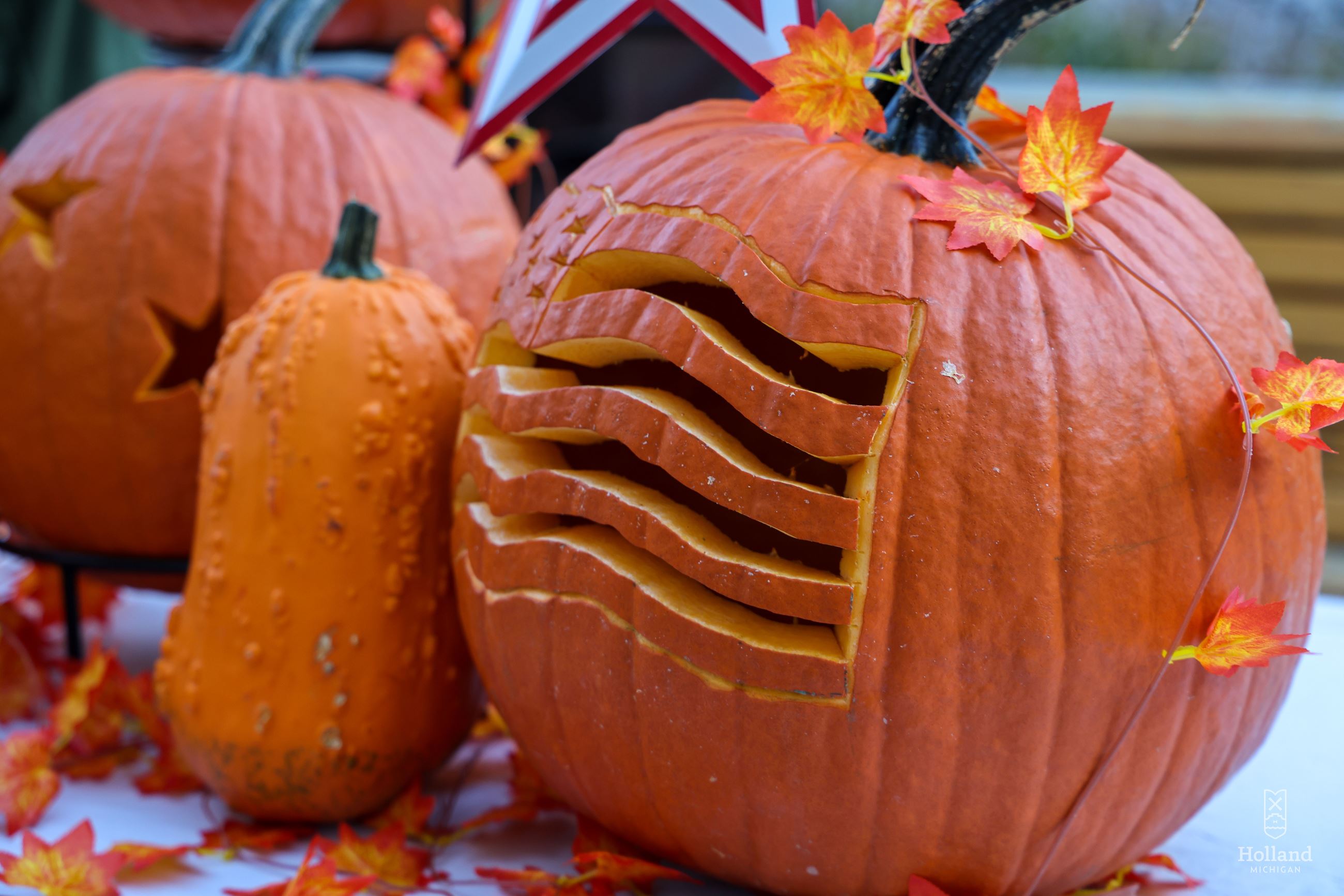 2 carved orange pumpkins and 1 orange gourd sitting on a table