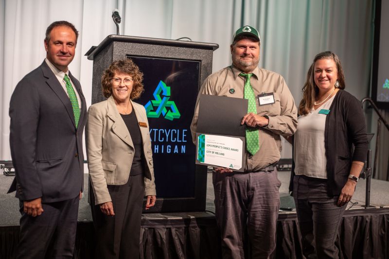 four adults, in business attire, standing in a row, one person holding a certificate 