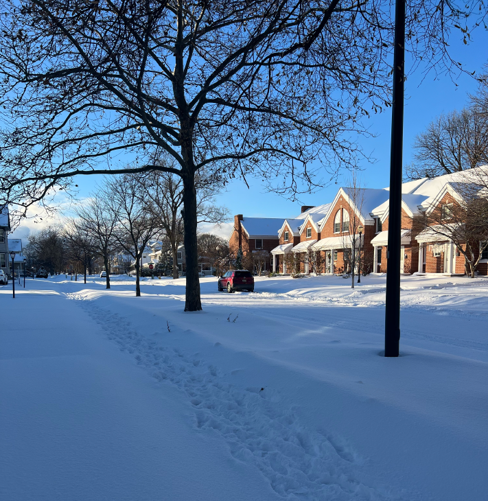 Snow covered sidewalk and street with buildings along the side and blue sky