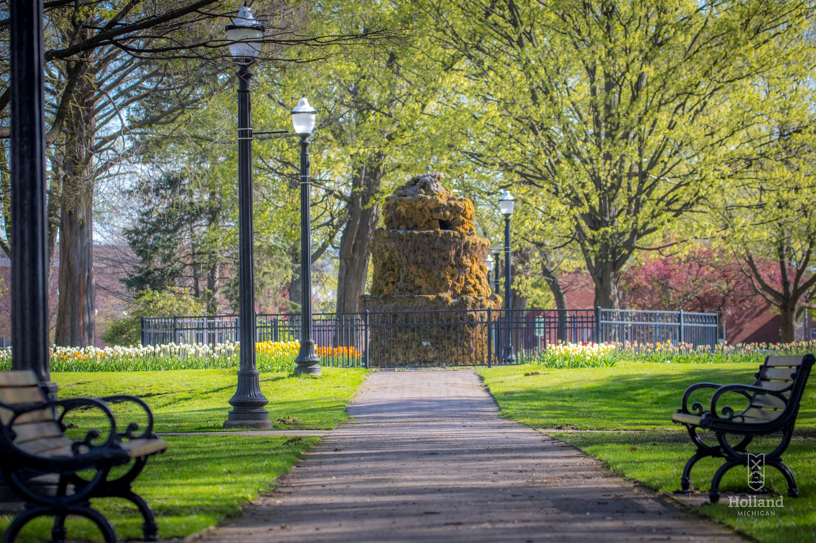 City Park with sidewalks and benches on either side and spring trees in the distance