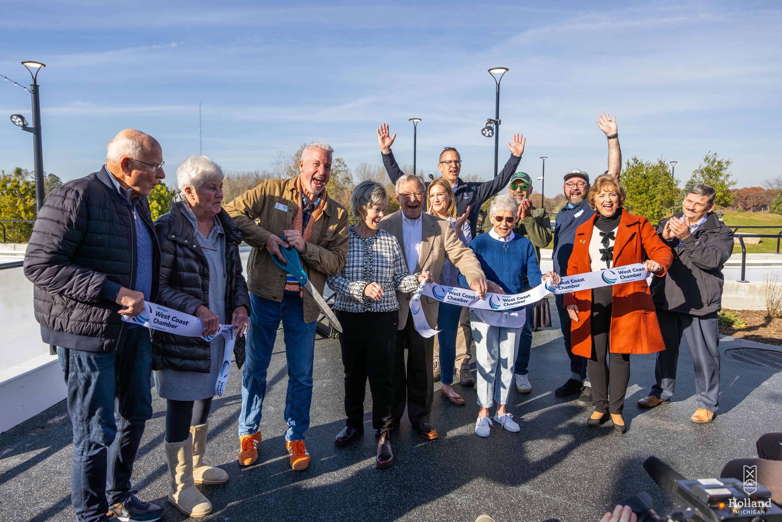Group of men and women officially cutting a ribbon with ice rink in background