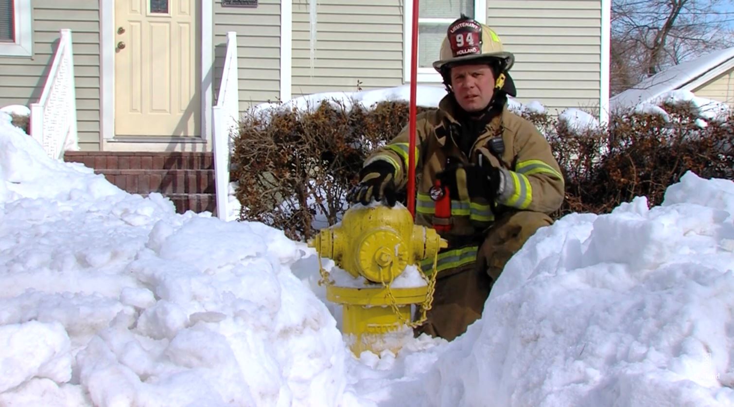 Firefighter kneeling next to a fire hydrant in deep snow in front of a home