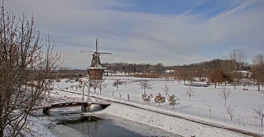 Snow covered ground overlooking a canal with large wooden bridge, Dutch windmill in background